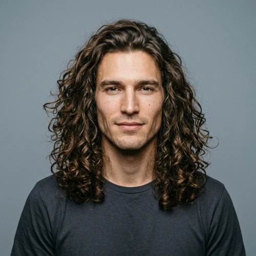 A 26-year-old man with long, voluminous wavy curly hair in a professional studio portrait.